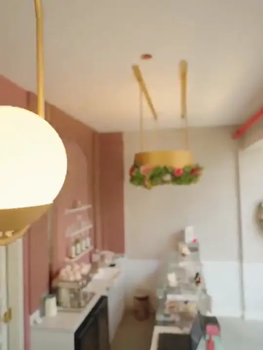 Balcão de confeitaria em rosa e branco com luminária globo e arranjo de flores suspenso