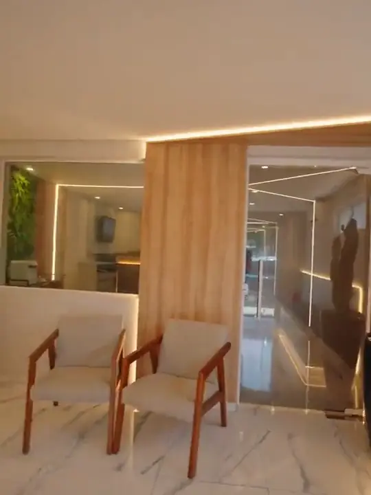Sala de espera de clínica odontológica com poltronas de madeira, painel ripado e piso de mármore