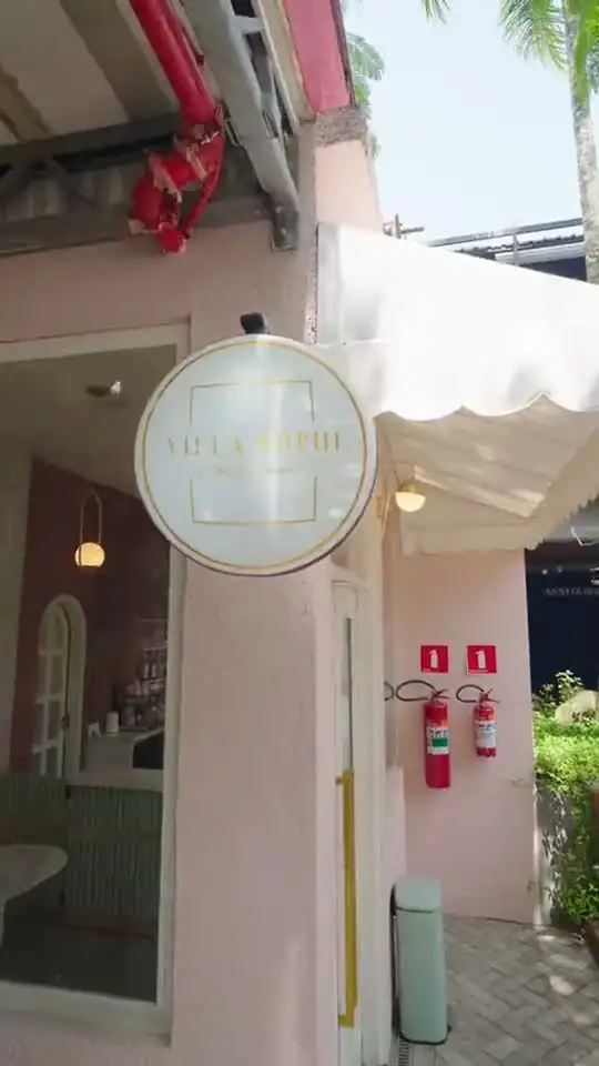 Fachada rosa de confeitaria com letreiro redondo, toldo branco e porta de vidro