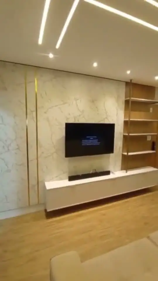 Sala de estar entregue com painel marmorizado, TV, rack branco e perfis de luz no forro