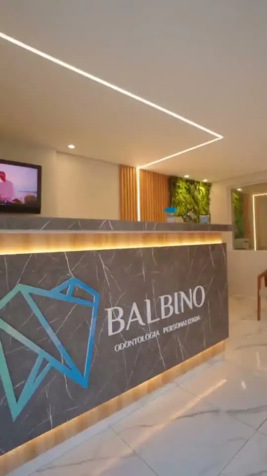 Recepção de clínica odontológica com balcão em pedra escura, fita de luz e jardim vertical ao fundo